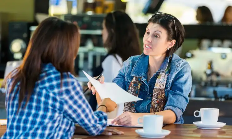 A woman interviews another woman at a coffee shop